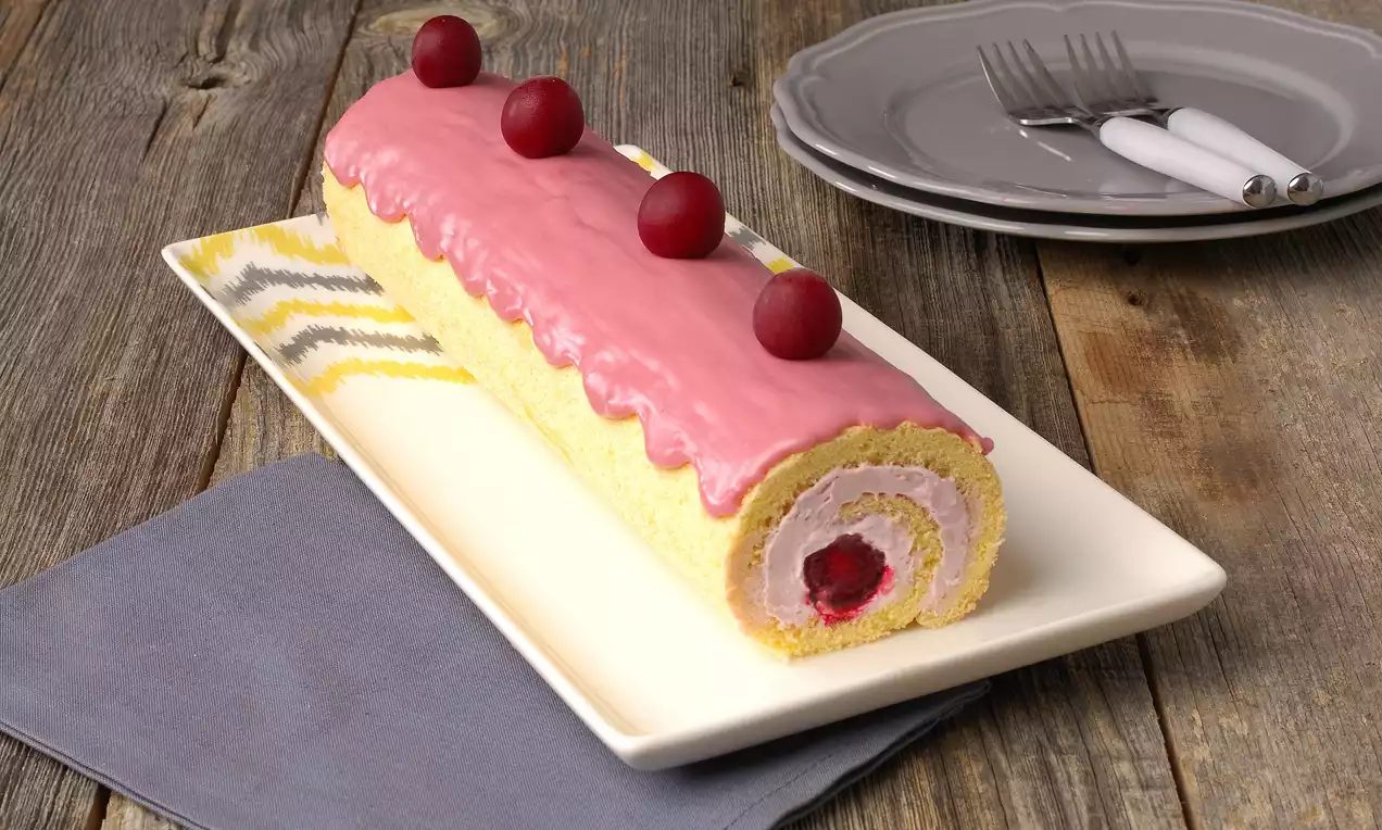 Sarı pandispanya keki, pembe vişneli glazürle kaplı, iç dolgusunda vişne parçaları olan, uzun dikdörtgen tabakta sunulmuş rulo pasta