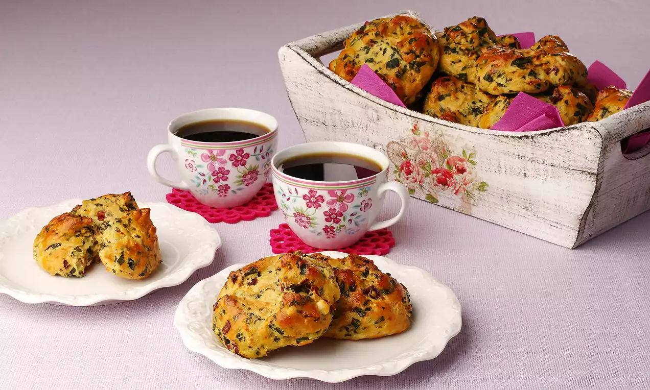 Ispanak ve baharatlarla hazırlanmış altın rengi ekmekçikler, beyaz tabaklarda ve çiçek desenli fincanlarla rustik bir sunumda yer alıyor
