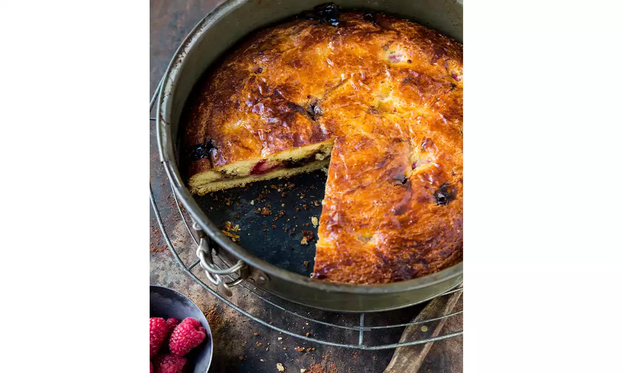 Goldbraune Ovotorte in Springform mit glänzender Oberfläche, fruchtigen Beerenstücken und einem herausgeschnittenen Tortenstück