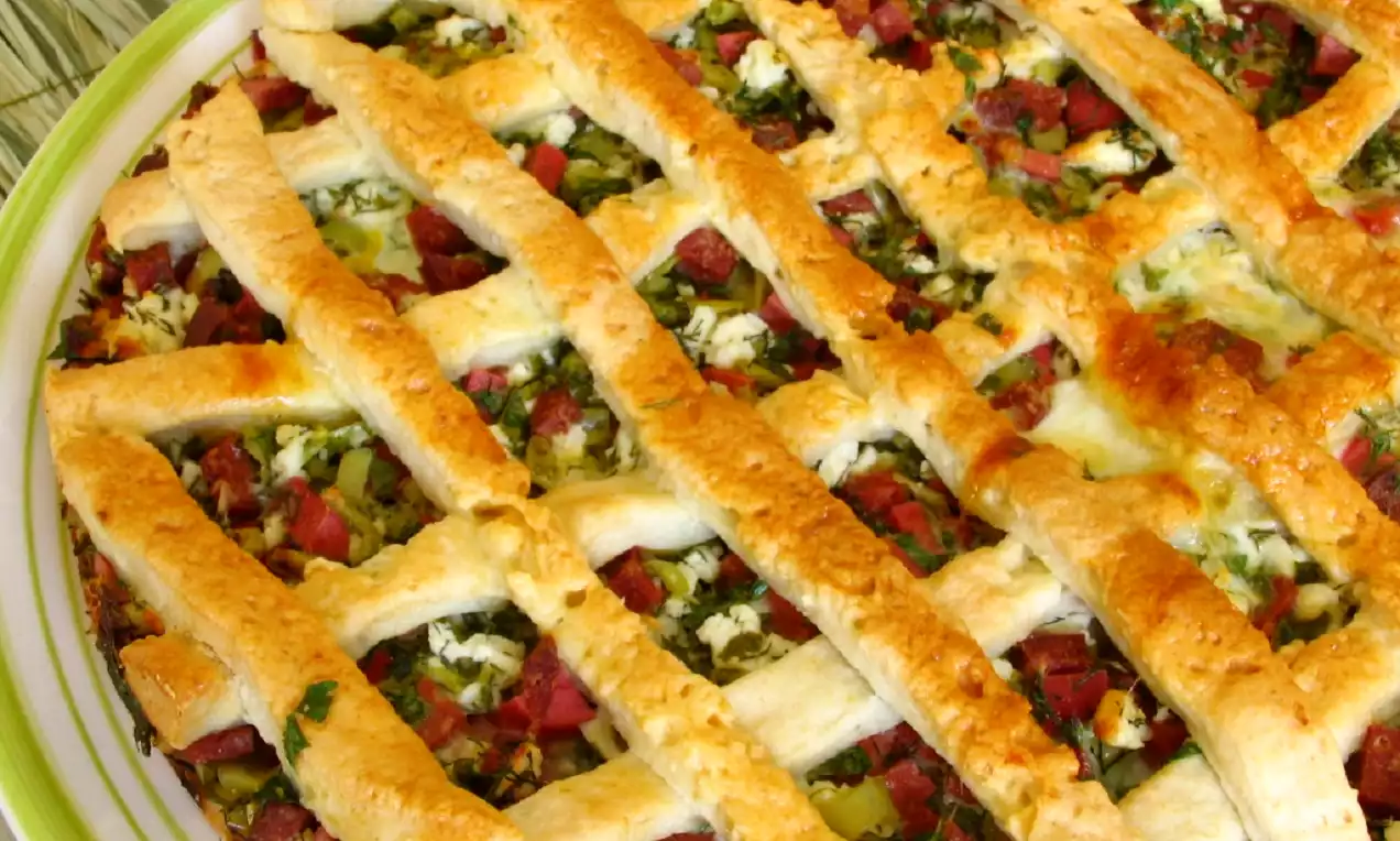 Altın rengi çıtır hamur şeritlerle örülü, üzerinde sucuk, beyaz peynir ve ince doğranmış maydanoz bulunan yuvarlak hamur işi