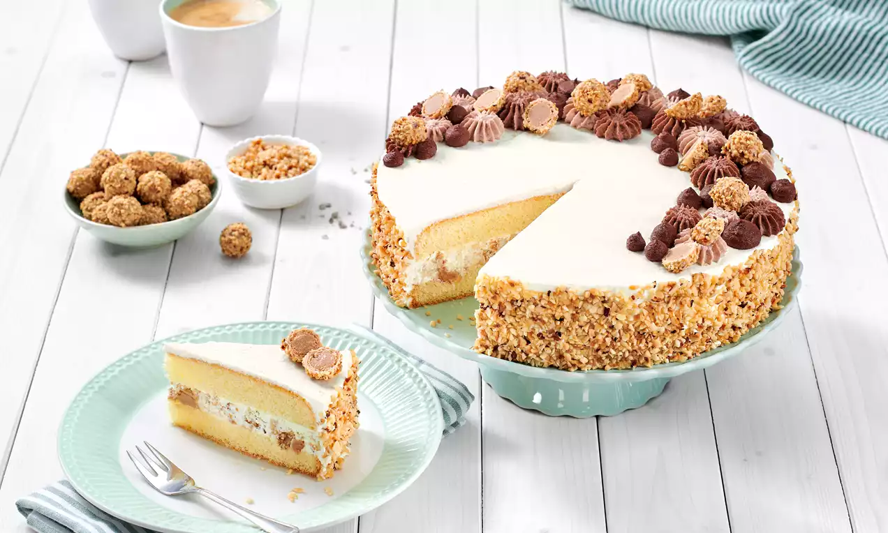 Giotto-Torte mit heller Creme, nussiger Krokant-Schicht und dekorativen Giotto-Kugeln auf Tortenteller, daneben ein Stück auf grünem Teller