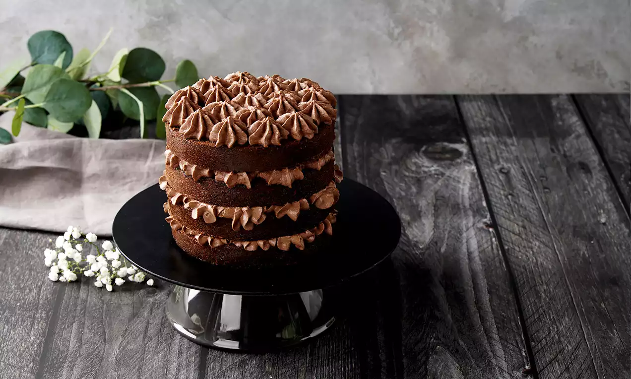Dunkler Schichtkuchen mit cremigen Schokoladentupfen zwischen den Lagen auf schwarzer Tortenplatte, dekoriert mit Eukalyptus und weißen Blüten