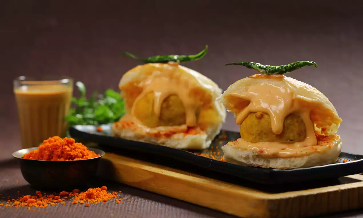 Golden crispy vadas resting inside soft white buns, topped with creamy orange chutney and green chilies on a black plate
