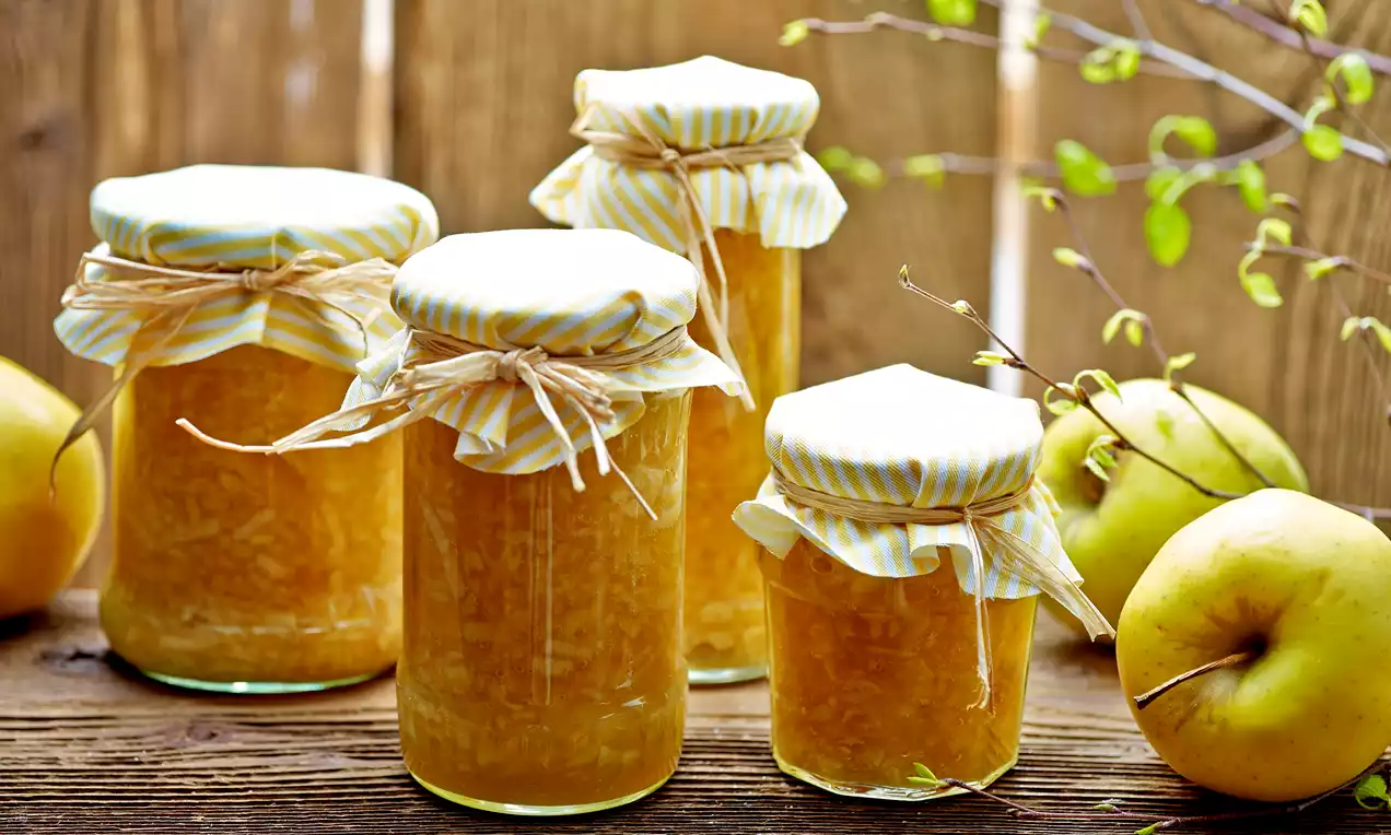 Pots de confiture dorée aux reflets orangés avec couvercles rayés en tissu et nœuds de ficelle, posés sur une table en bois rustique