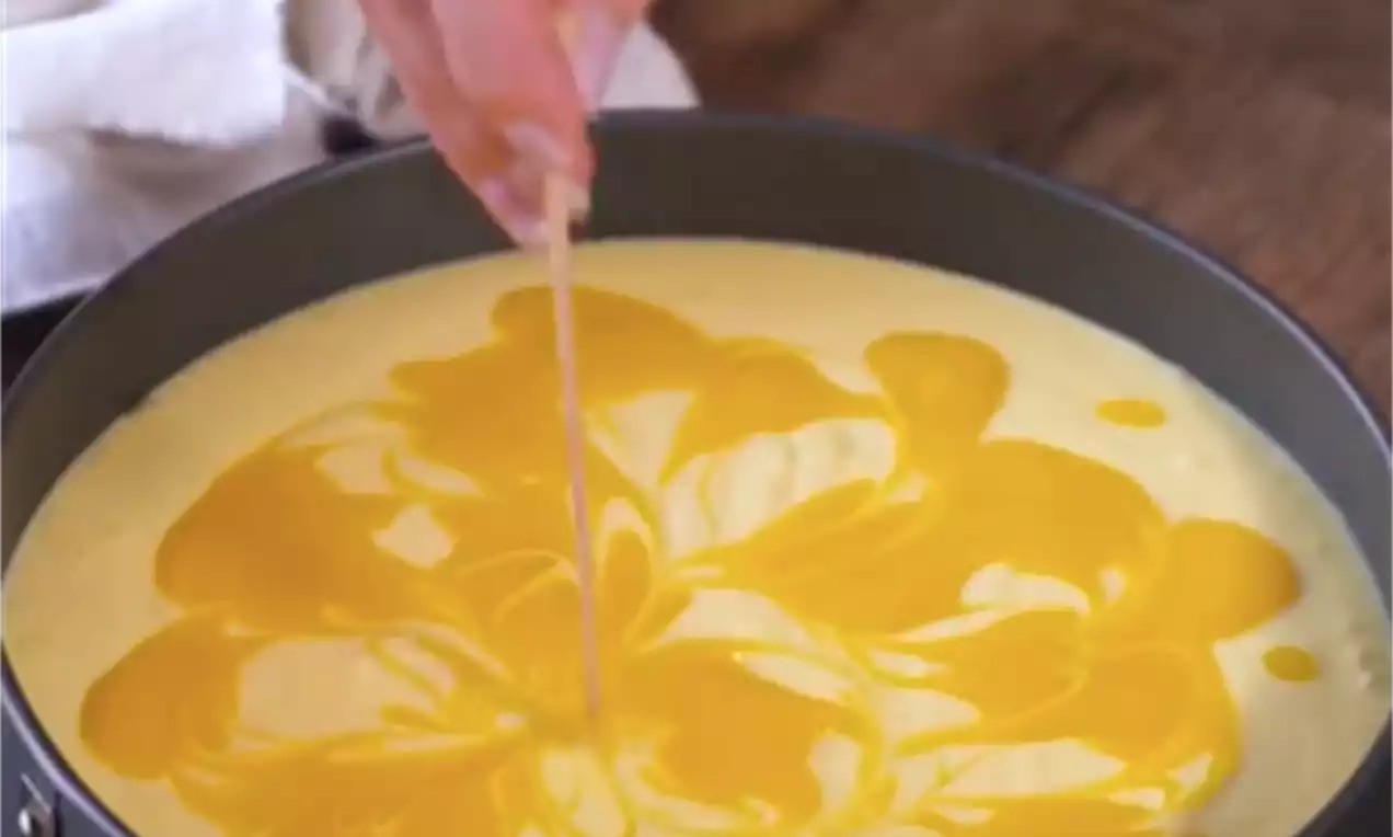 Mangova torta v pekaču z gladko rumeno površino in marmoriranim vzorcem svetlo oranžne barve, oblikovanim s tanko paličico