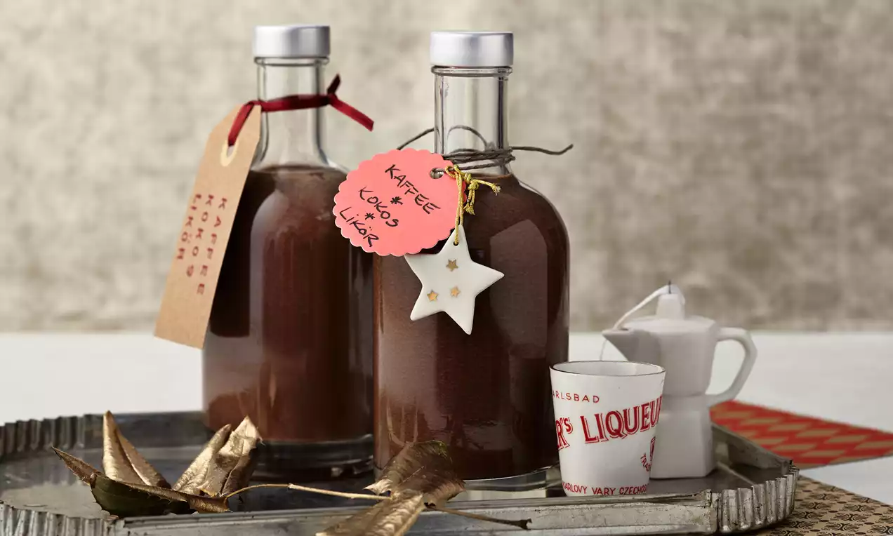 Zwei klare Glasflaschen mit braunem Kaffee-Kokos-Likör, verziert mit Anhängern und Sternendekoration, auf einem silbernen Tablett mit kleinen Beigaben