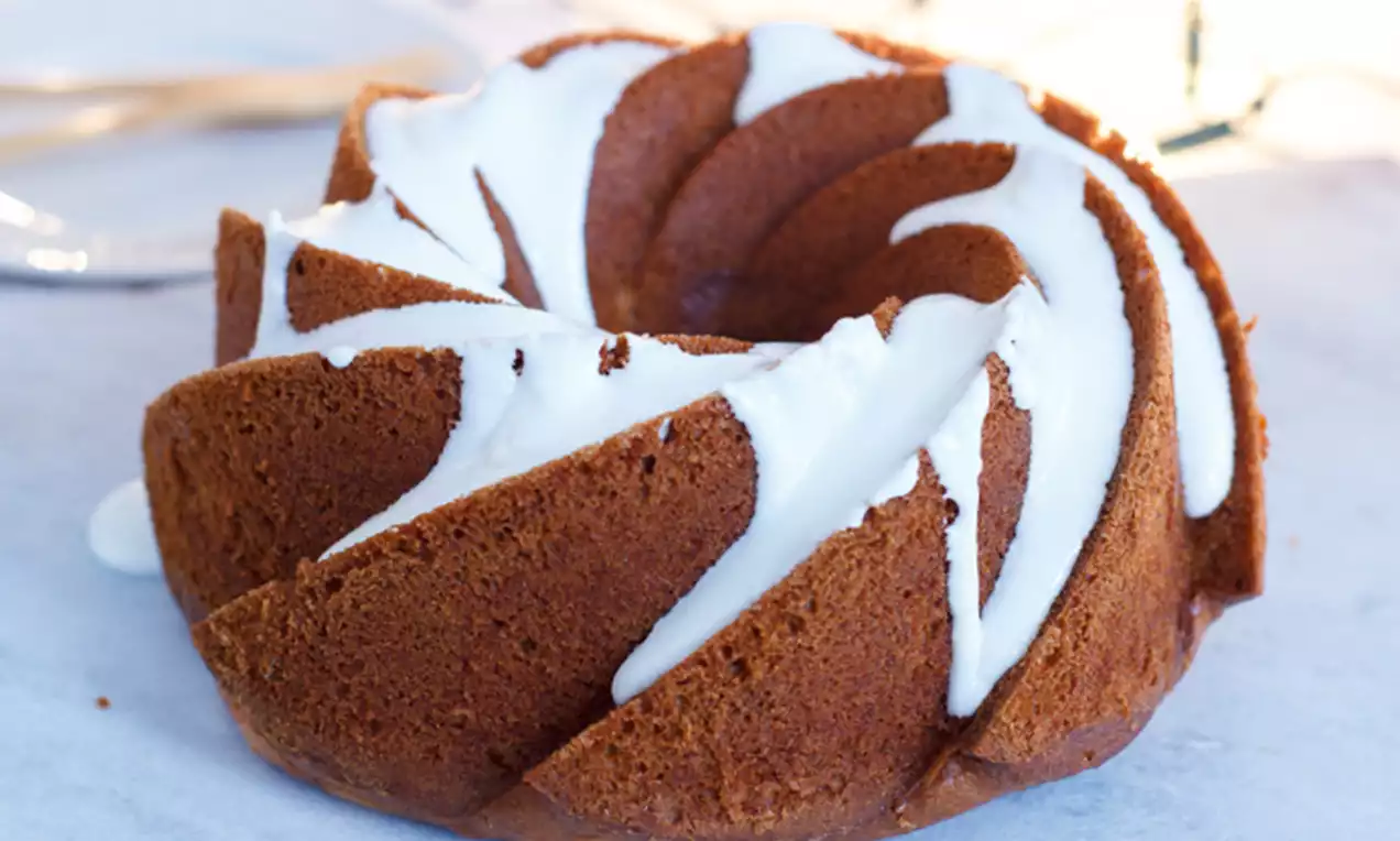 Gespiraliseerde bundtcake met warme karamelkleur en romige witte glazuurstrepen, gepresenteerd op een lichtblauw stenen oppervlak