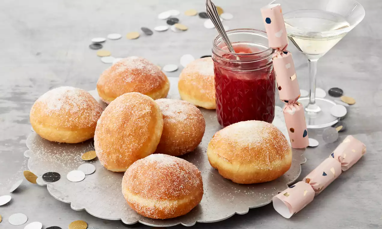 Berliner goldbraun und locker, mit Puderzucker bestäubt und gefüllt mit roter Konfitüre, auf weißem Teller dekorativ arrangiert