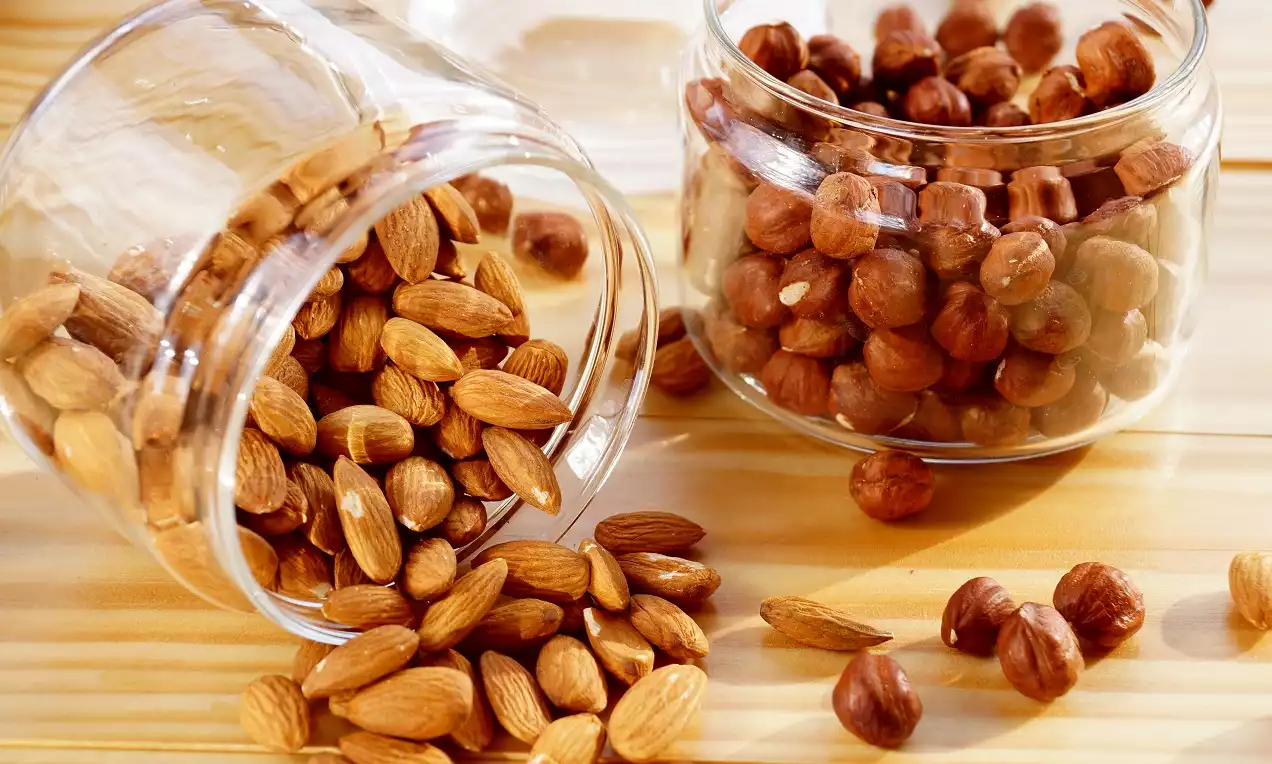 Cam kavanozlara yerleştirilmiş bütün bademler ve fındıklar, ahşap yüzey üzerinde dağınık şekilde sergilenmiş