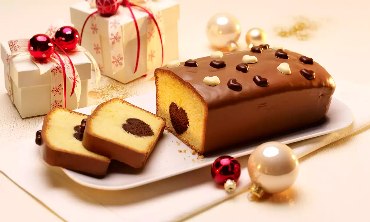 Ciasto waniliowe o gładkiej, błyszczącej polewie czekoladowej, z wnętrzem w kształcie serca, udekorowane czekoladowymi motywami na białej paterze