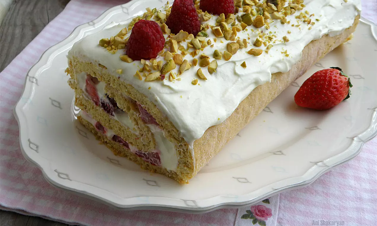 Руло от светъл пандишпан със сметанов крем, розови малини и натрошени шамфъстъци, украсено със свежи малини върху порцеланова чиния