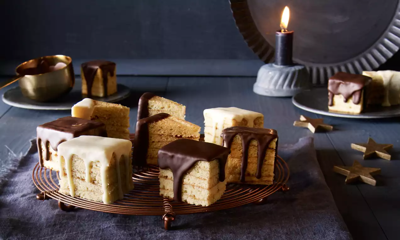 Réteges négyzet alakú sütemények csokoládé- és cukormázzal, rácson elrendezve sötét háttér előtt, mécses és csillag díszekkel