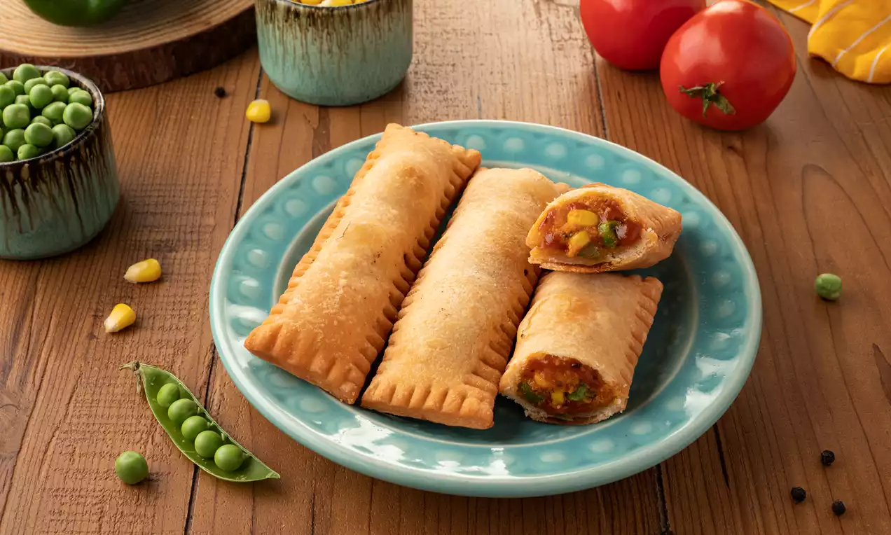 Golden brown rectangular pastry pockets with crimped edges, one cut open to reveal vibrant vegetable filling on a turquoise plate