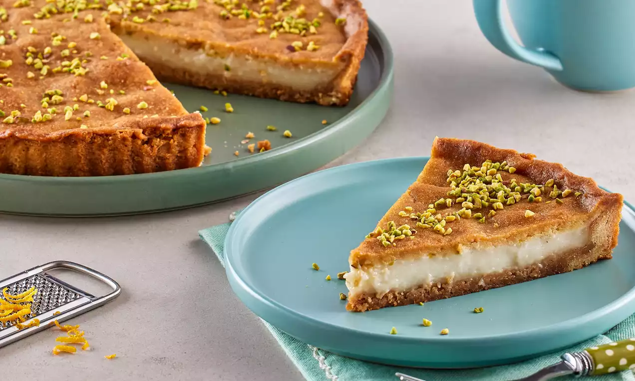 Altın rengi ince hamur tabanlı, beyaz tavukgöğsü dolgulu, üzeri hafif kızarmış ve ince Antep fıstığı parçalarıyla süslenmiş dilim tart