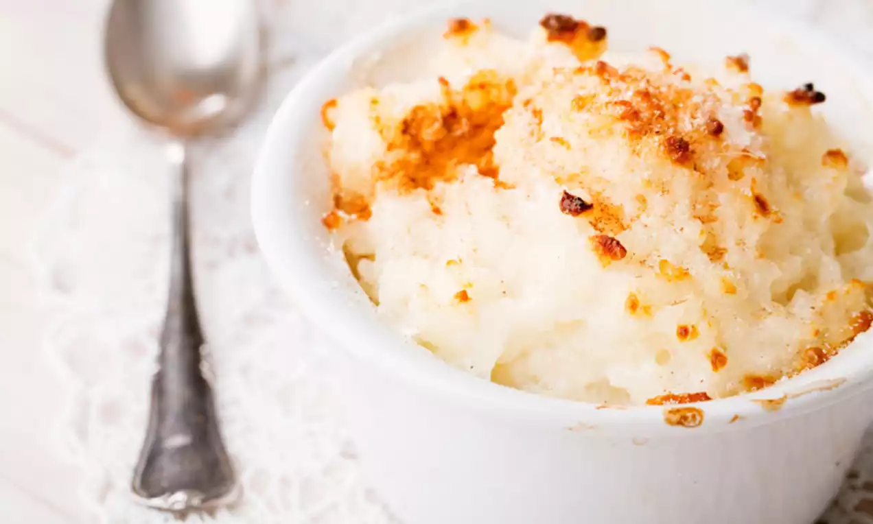Coconut rice pudding with golden crispy topping in a white ramekin on a lace-trimmed surface beside an antique silver spoon