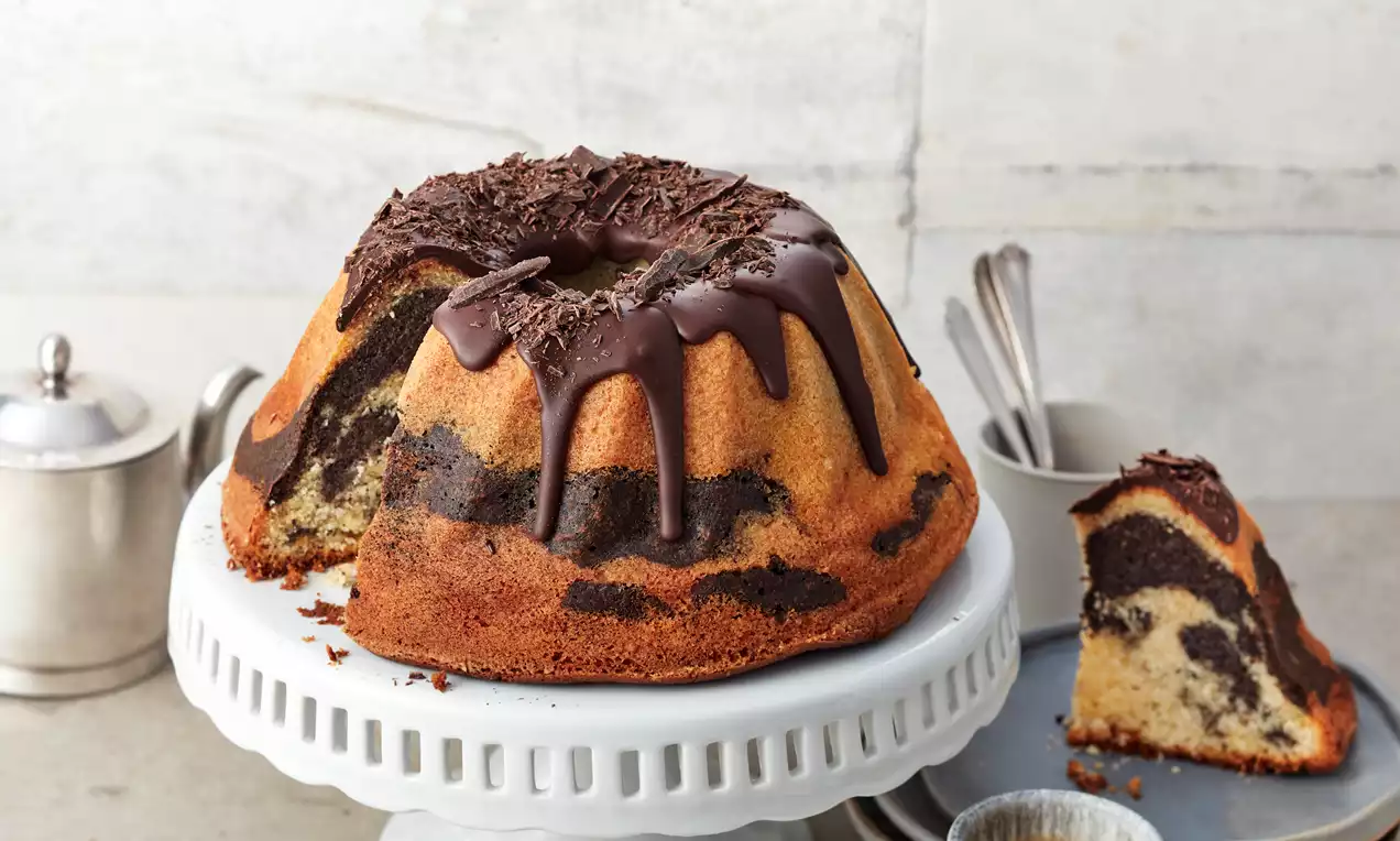 Mohn-Eierlikör-Kuchen in Gugelhupfform mit glänzender Schokoglasur, Mohnfüllung sichtbar und leicht bestäubt, auf weißem Teller