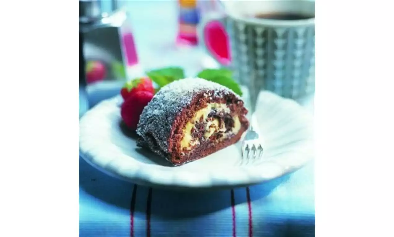 Mørk sjokoladerulle med lys kremfyll, drysset med melis, servert på hvit tallerken med bringebær og grønn mynteblad ved siden av