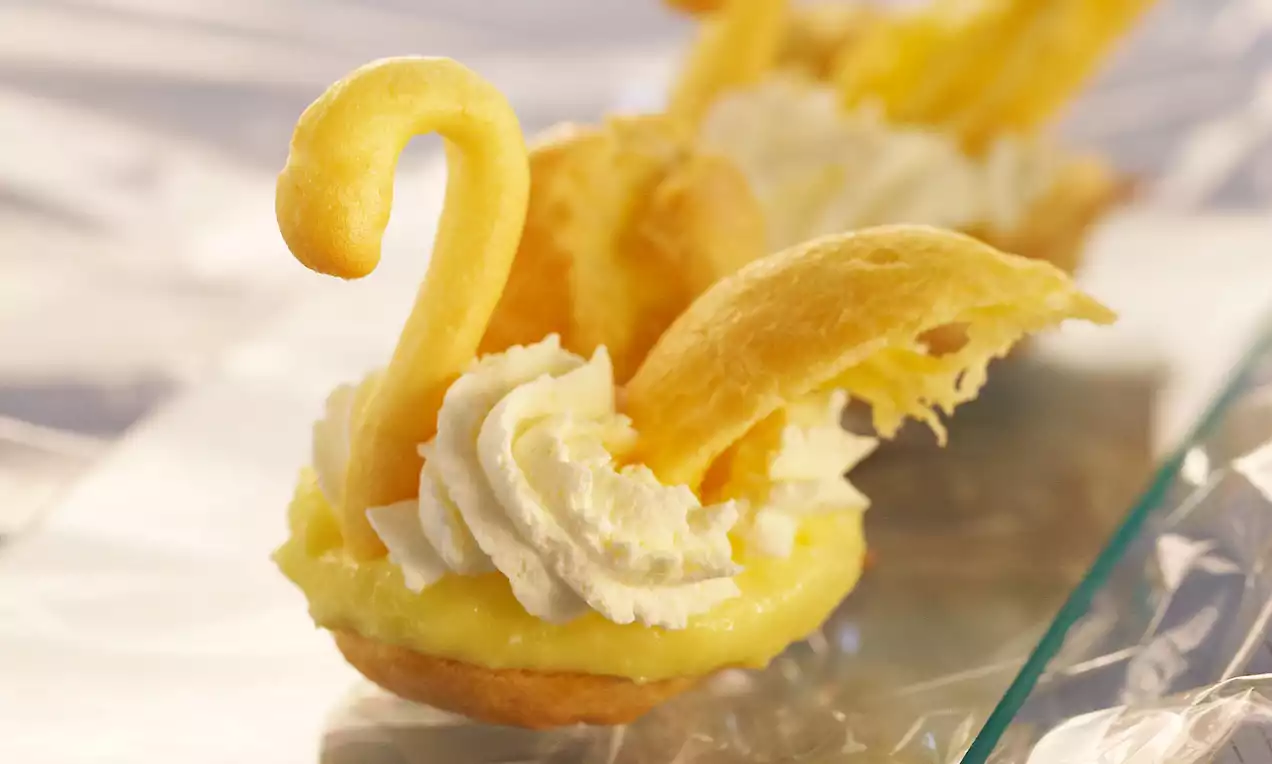 Petits cygnes en pâte à choux dorée avec une crème blanche légère et onctueuse sur une base garnie d’une crème jaune pâle
