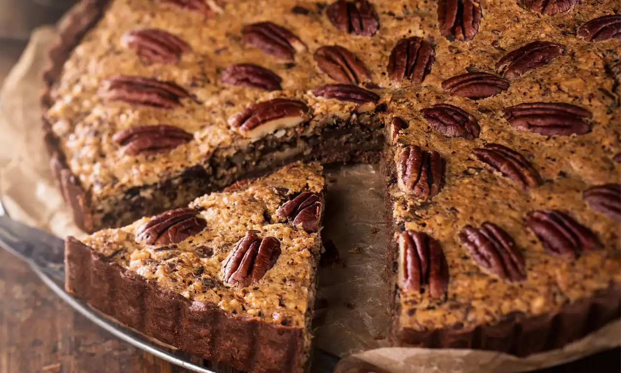 Pecan-Schoko-Pie mit nussbrauner Füllung, einzeln platzierten Pecannüssen auf knusprigem Rand, angeschnitten auf braunem Backpapier