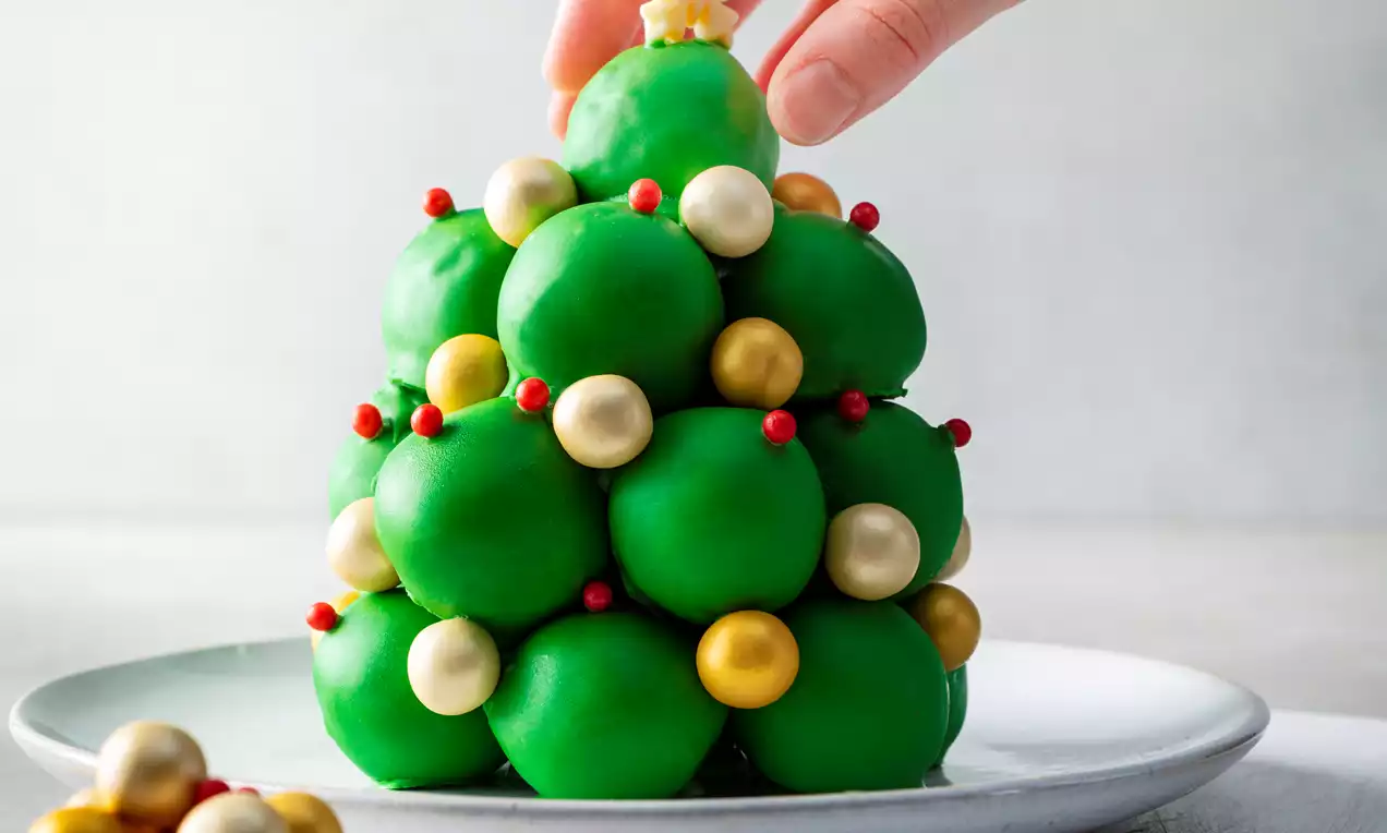 Sapin de Noël en cake pops verts entassés en pyramide, décorés de perles dorées et rouges avec une étoile en biscuit au sommet