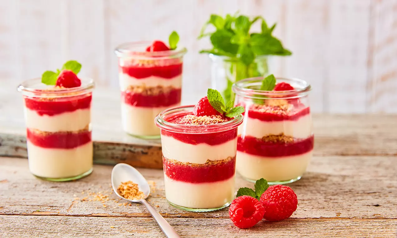 Кремообразен кокосов пудинг в прозрачно стъклено бурканче, на пластове с яркочервен малинов слой, гарниран с пресни малини и зелена мента