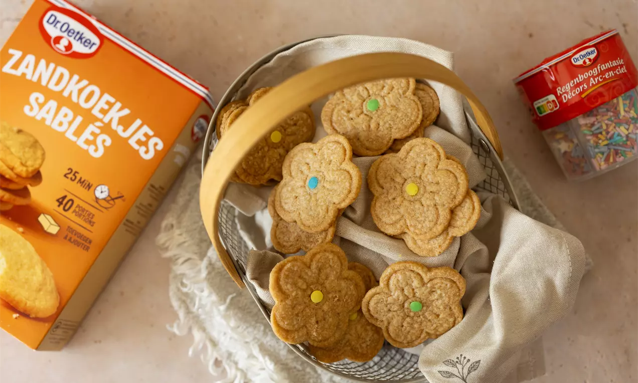 Bloemvormige zandkoekjes met een gouden kleur en kleurrijke snoepjes in het midden, gerangschikt in een mandje met een linnen doek