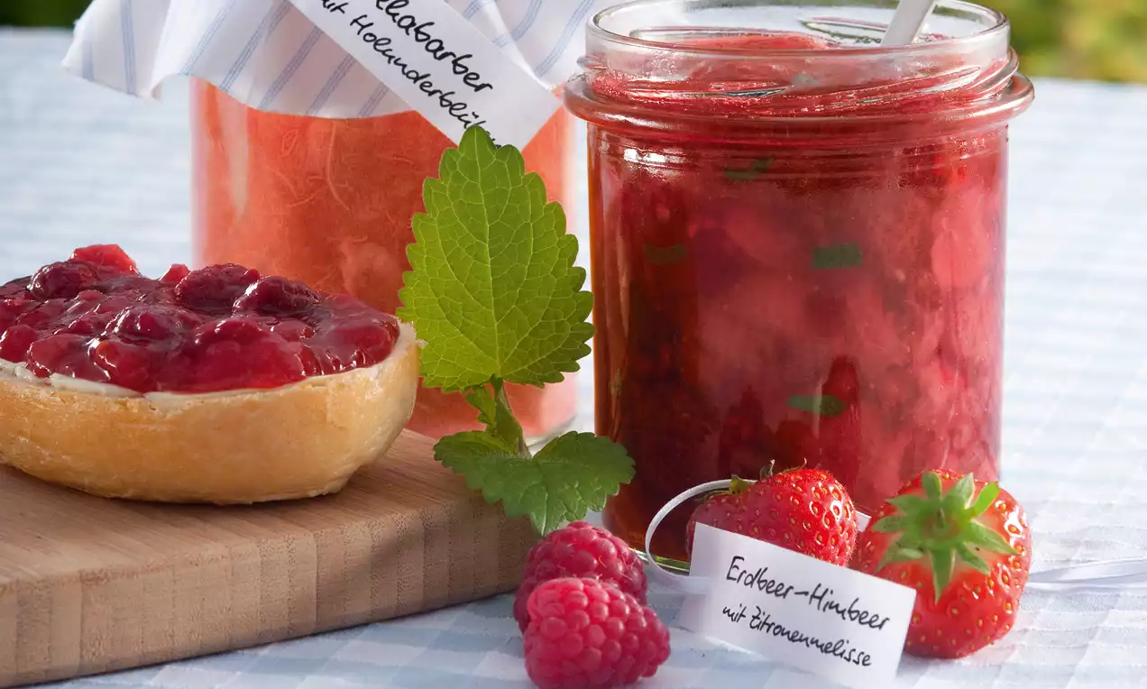 Confiture rouge brillante au sureau dans un pot en verre, accompagnée de framboises, fraises et rondelle croustillante garnie