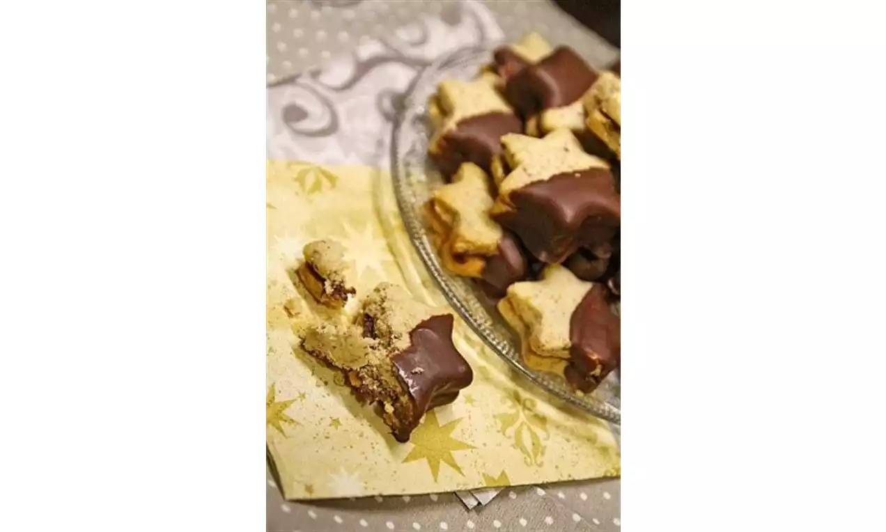 Galletas en forma de estrella de masa dorada con puntas bañadas en chocolate oscuro, dispuestas sobre un plato de cristal y un mantel decorado