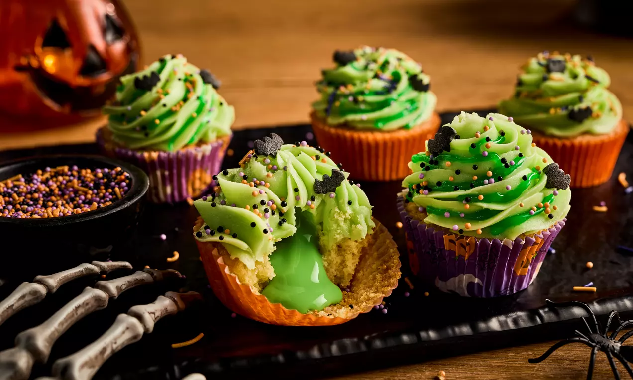 Bright green slime cupcakes with swirled frosting, colourful sprinkles and gooey lime-green filling against a Halloween-themed setting