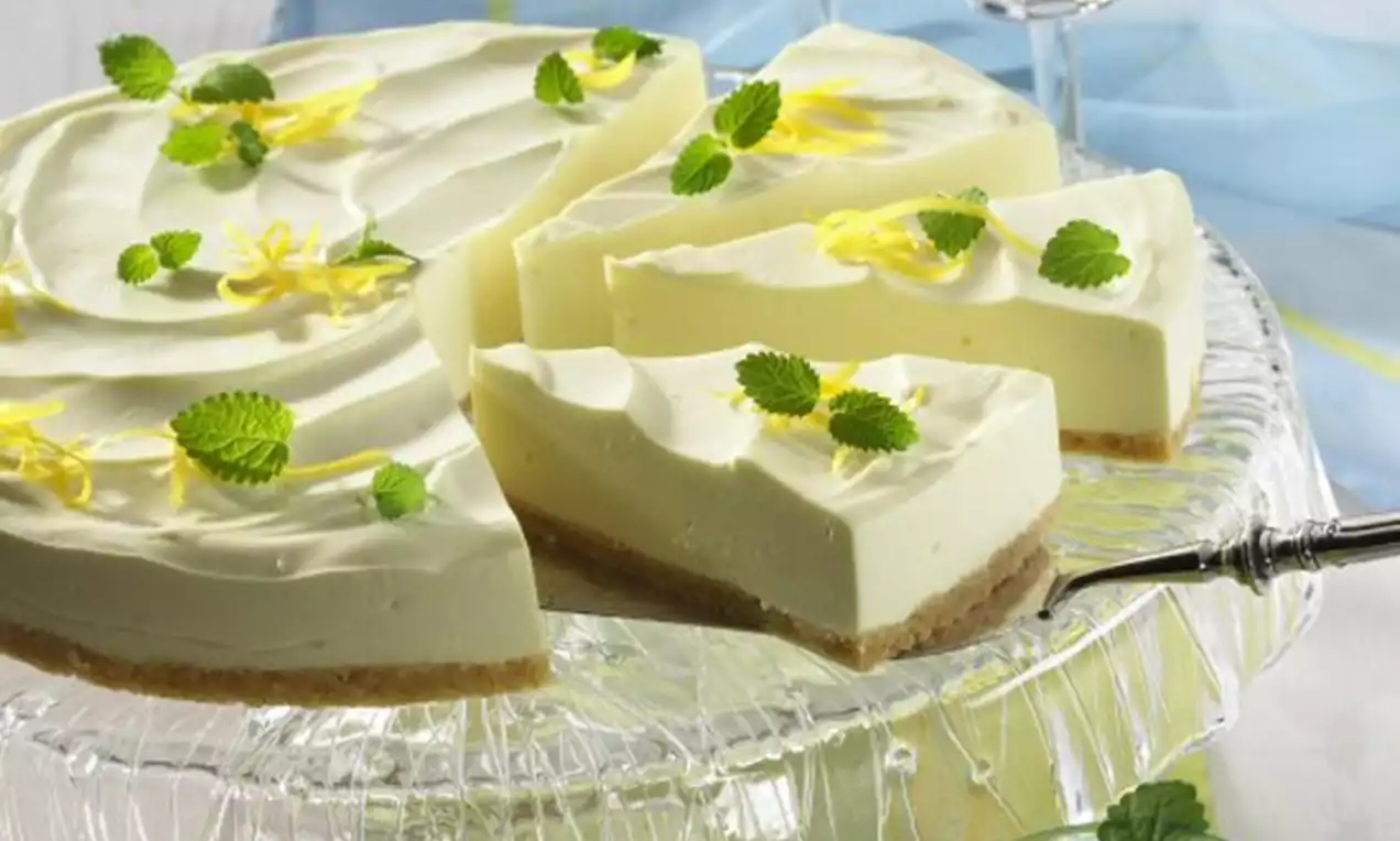 Limettentorte mit glatter Creme auf goldenem Keksboden, garniert mit Zitronenzesten und grünen Blättern auf einer Glasplatte