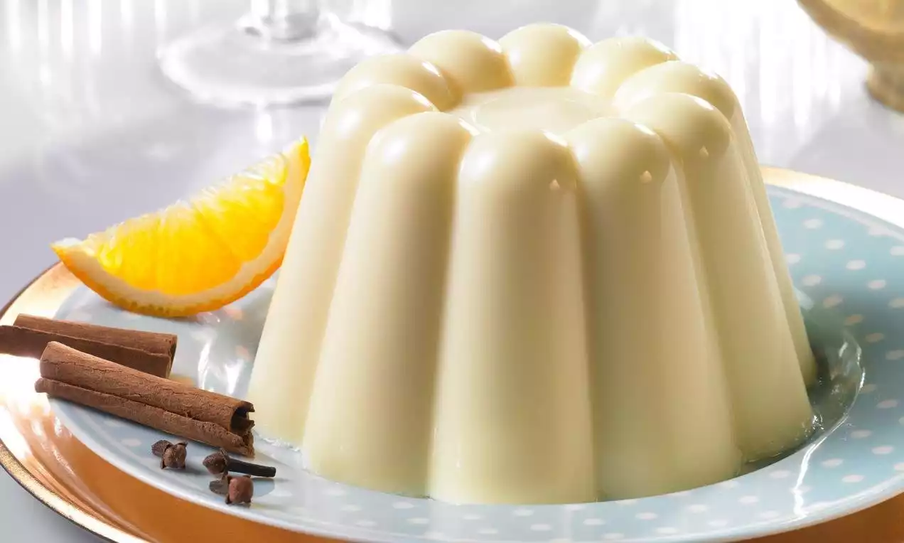 Pudding à la vanille lisse et pâle en forme de moule à cannelures sur une assiette à pois avec tranche d'orange et bâtons de cannelle