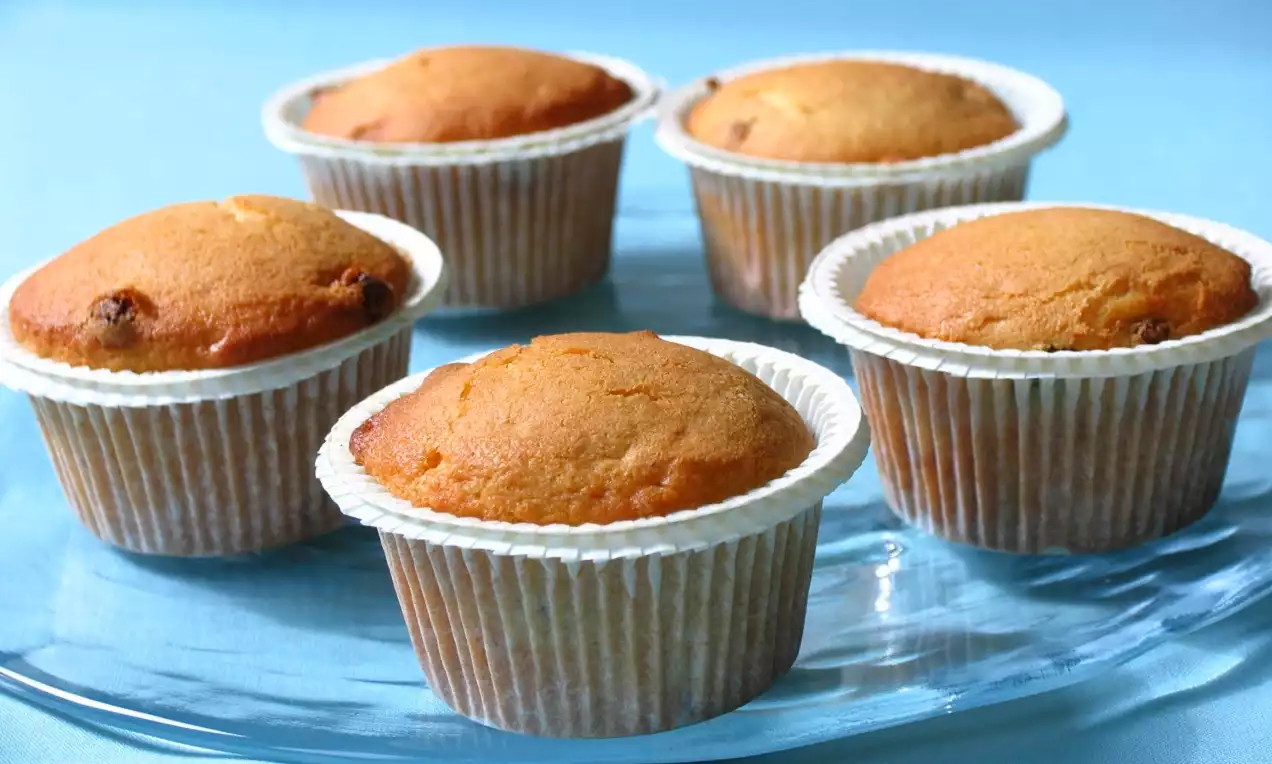 Altın rengi üst yüzeyleri hafif kabarık, beyaz kağıt kalıplar içinde düzenli şekilde yerleştirilmiş beş muffin cam bir tabakta