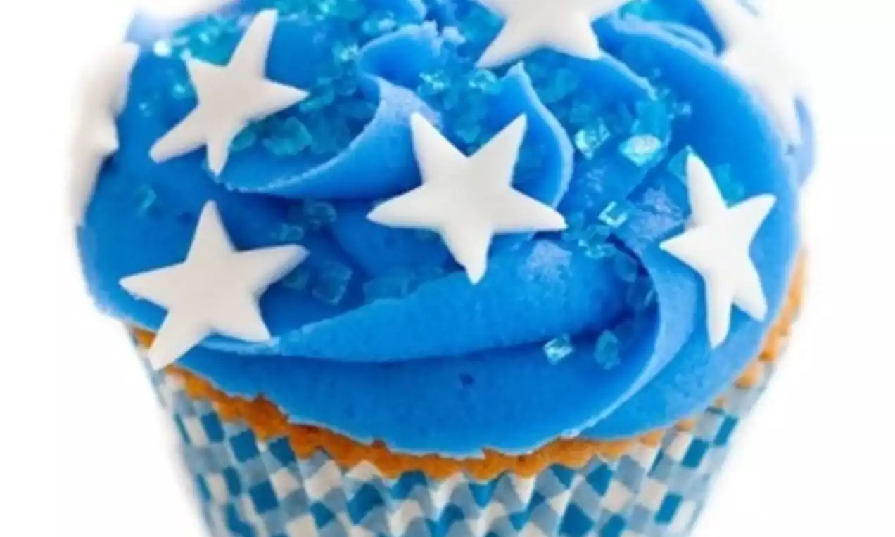 Cupcake met luchtige felblauwe crème, versierd met witte stervormige decoraties en suikerparels in een blauw-wit geblokte papieren omhulsel