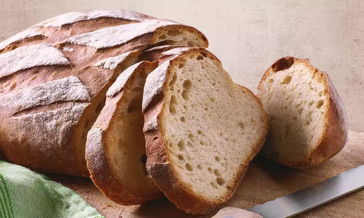 Mischbrot mit goldbrauner Kruste, geschnitten in dicke Scheiben mit luftiger Textur auf einem Holzbrett neben einem grünen Stofftuch