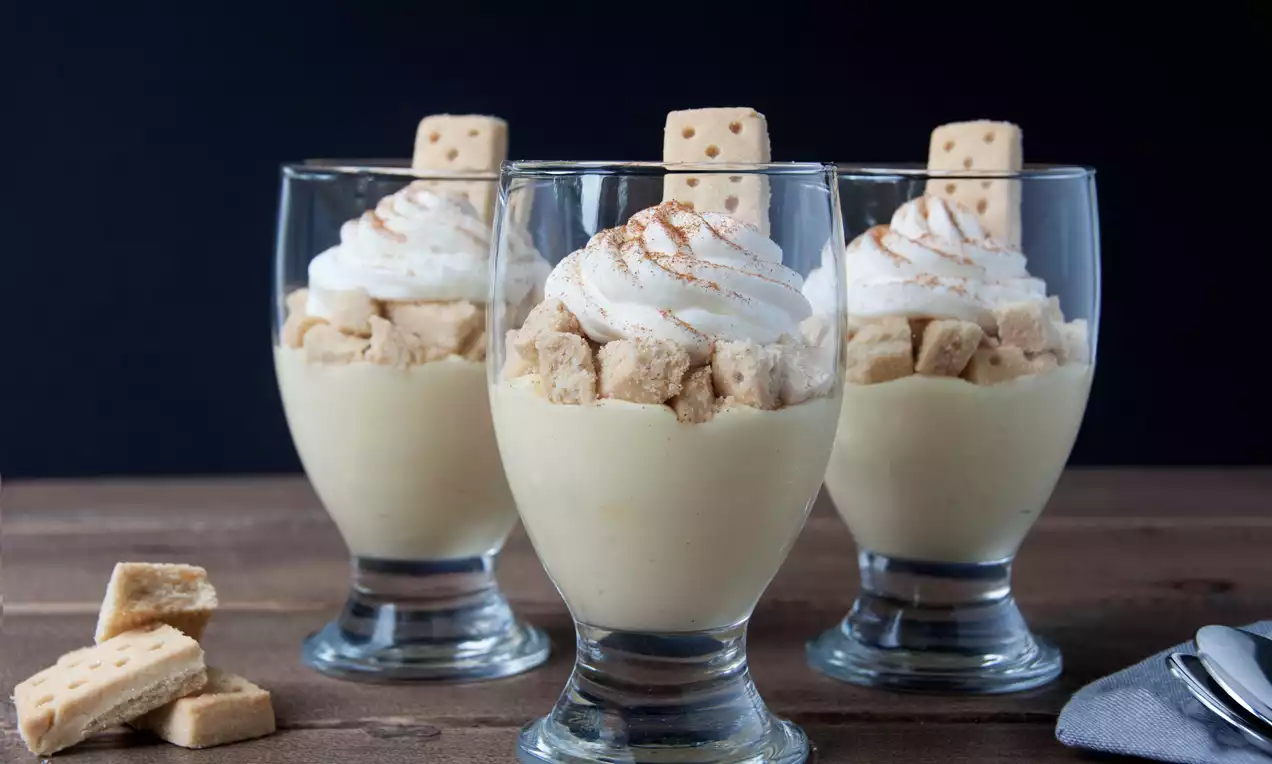 Dessert crémeux beige en verrines transparentes, garni de morceaux de sablés dorés, chantilly blanche et trait de cannelle