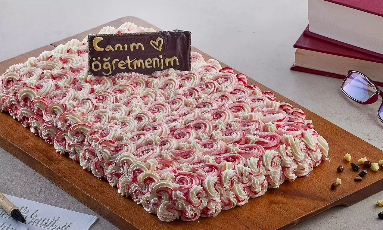 Kırmızı ve beyaz tonda kıvrımlı kremalarla süslenmiş dikdörtgen pasta, ahşap sunum tahtasında yazılı çikolata ile dekor edilmiş