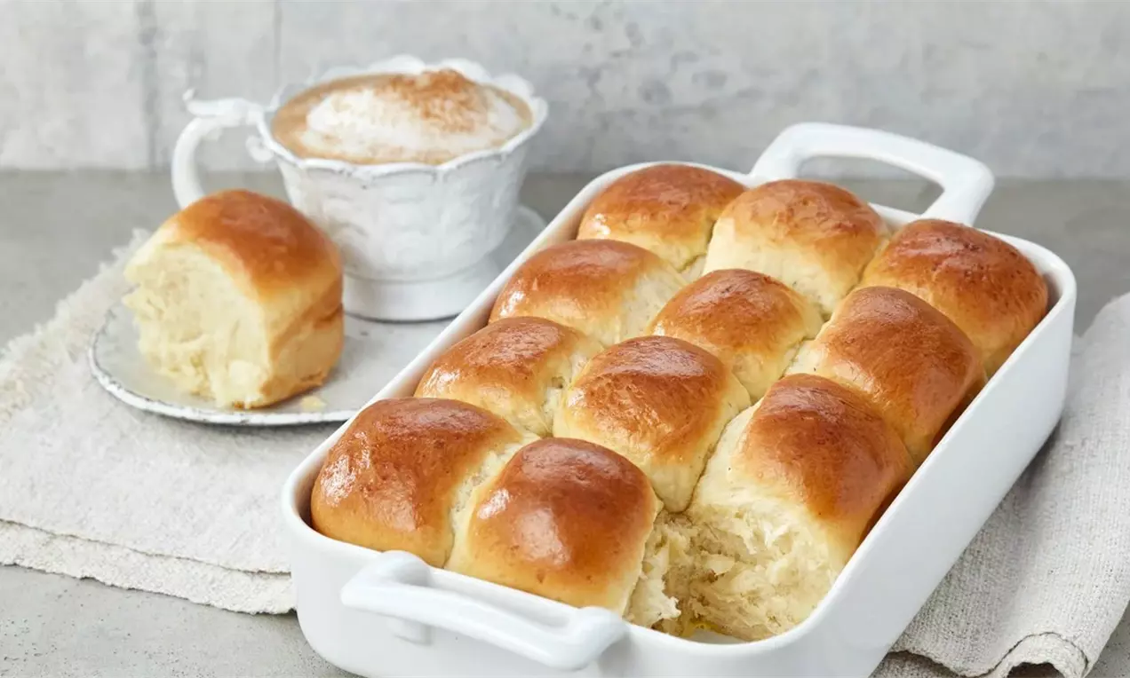 Златисти квадратни питки с мека и пухкава текстура, подредени плътно в правоъгълна бяла тава върху светъл плат