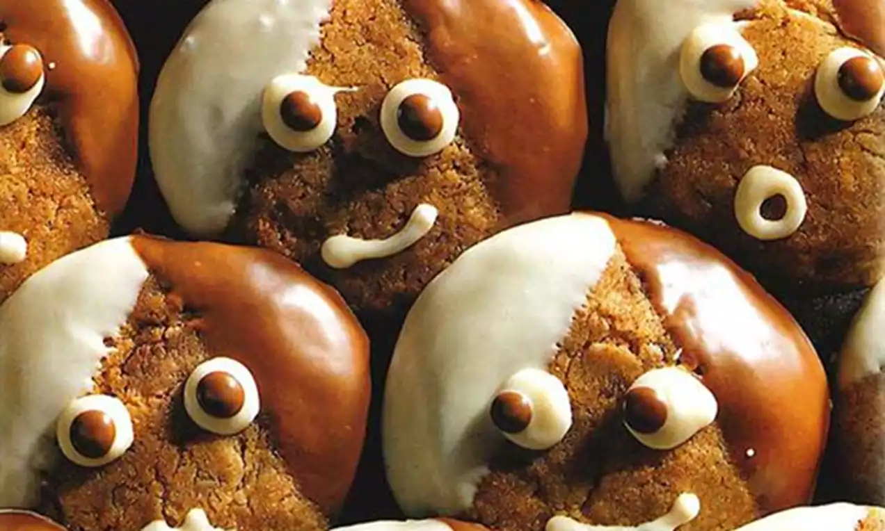 Petits biscuits ronds dorés à moitié nappés de chocolat blanc et brun, décorés de visages souriants aux yeux et bouches en chocolat