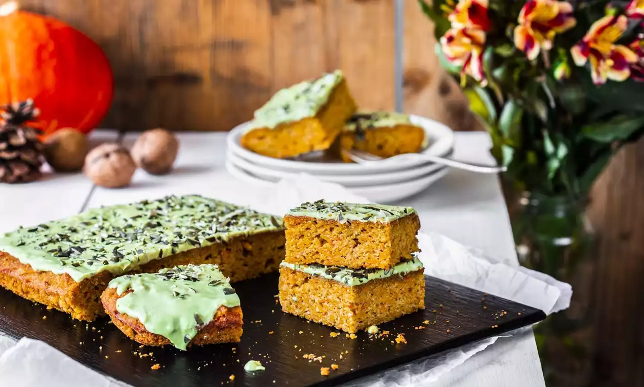Barritas rectangulares de bizcocho anaranjado con glaseado verde claro y trozos de chocolate, dispuestas sobre una bandeja negra