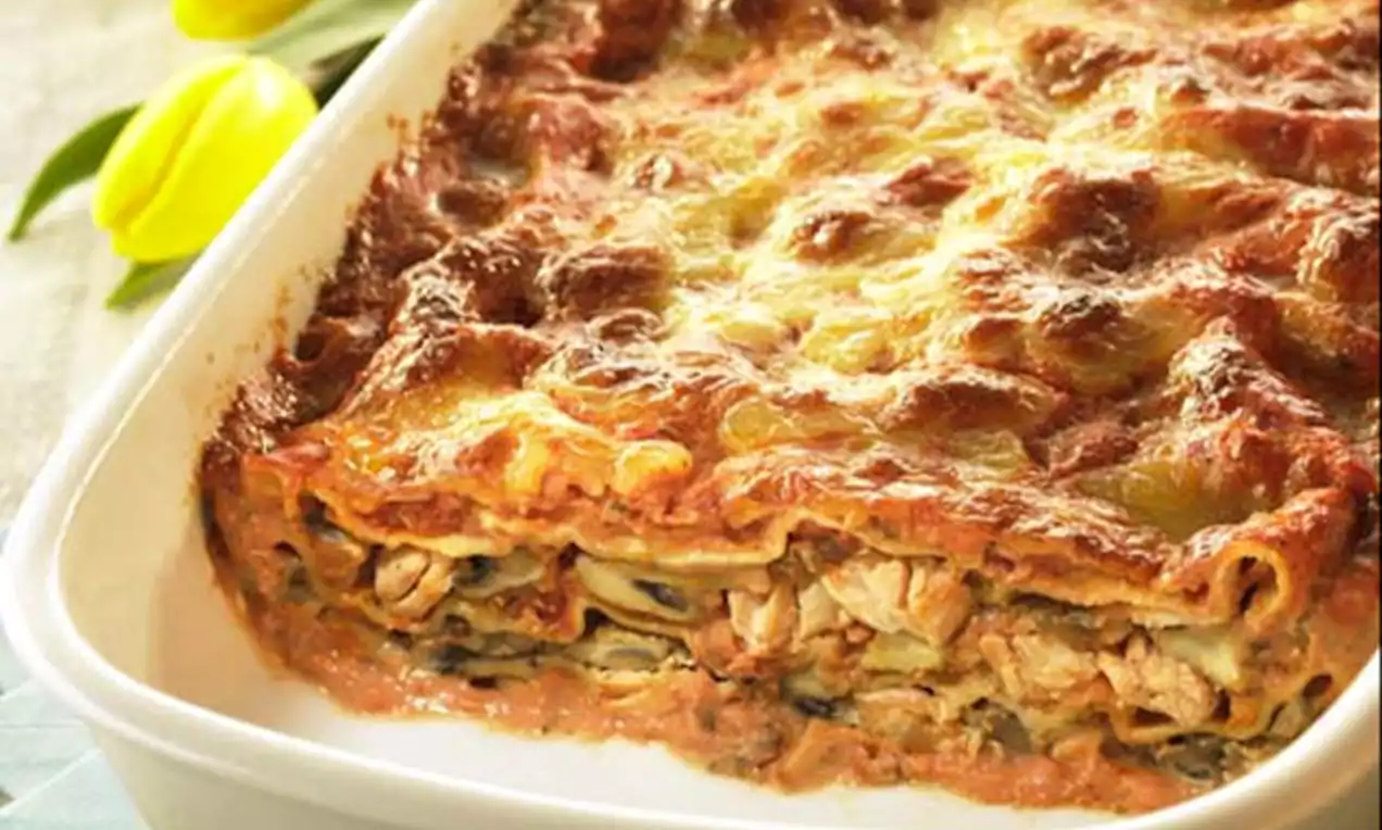 Goldbraune Lasagne mit geschmolzener Kruste und sichtbaren Schichten von hellen Nudeln und cremiger Füllung in weißer Auflaufform