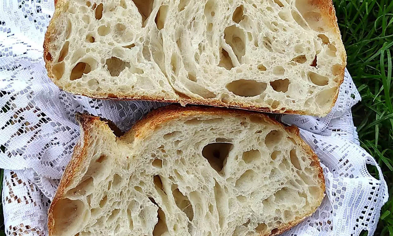 Durum kruh s hrskavom zlatnosmeđom koricom i prozračnom svijetlom unutrašnjosti, položen na bijeli čipkasti ubrus na zelenoj travi