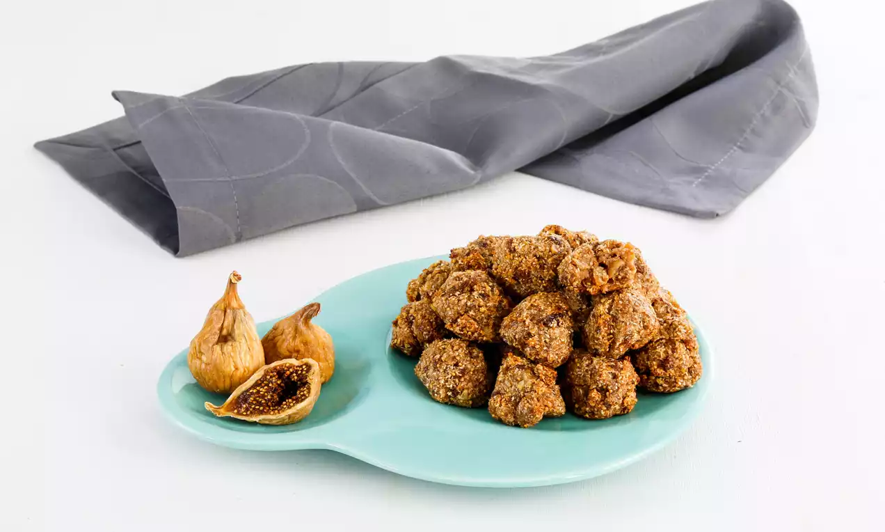 Küçük taneli ve pürüzlü yüzeyli kurabiyeler, turkuaz tabakta kurutulmuş ve ortadan kesilmiş incirlerle birlikte düzenlenmiş