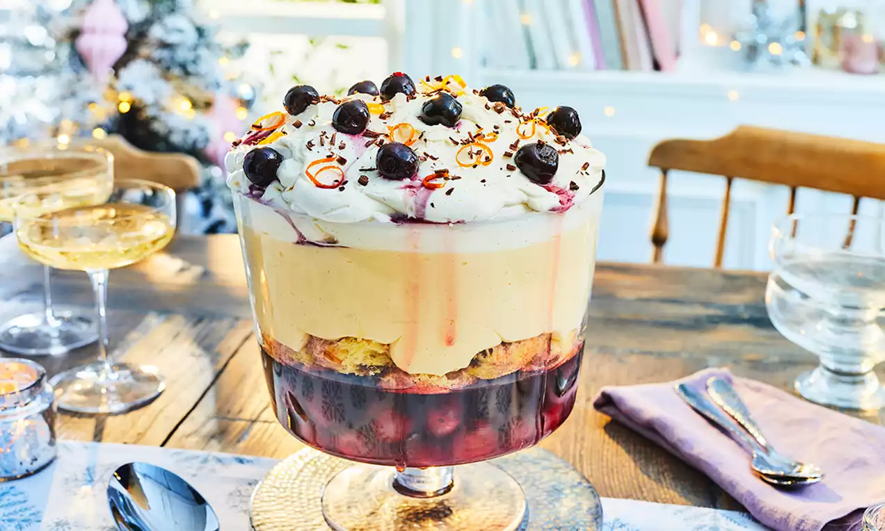 Trifle Panettone stratificat, cu bază roșu intens de fructe, prăjitură aurie, cremă catifelată vanilie și frișcă decorată cu vișine și coajă de portocală