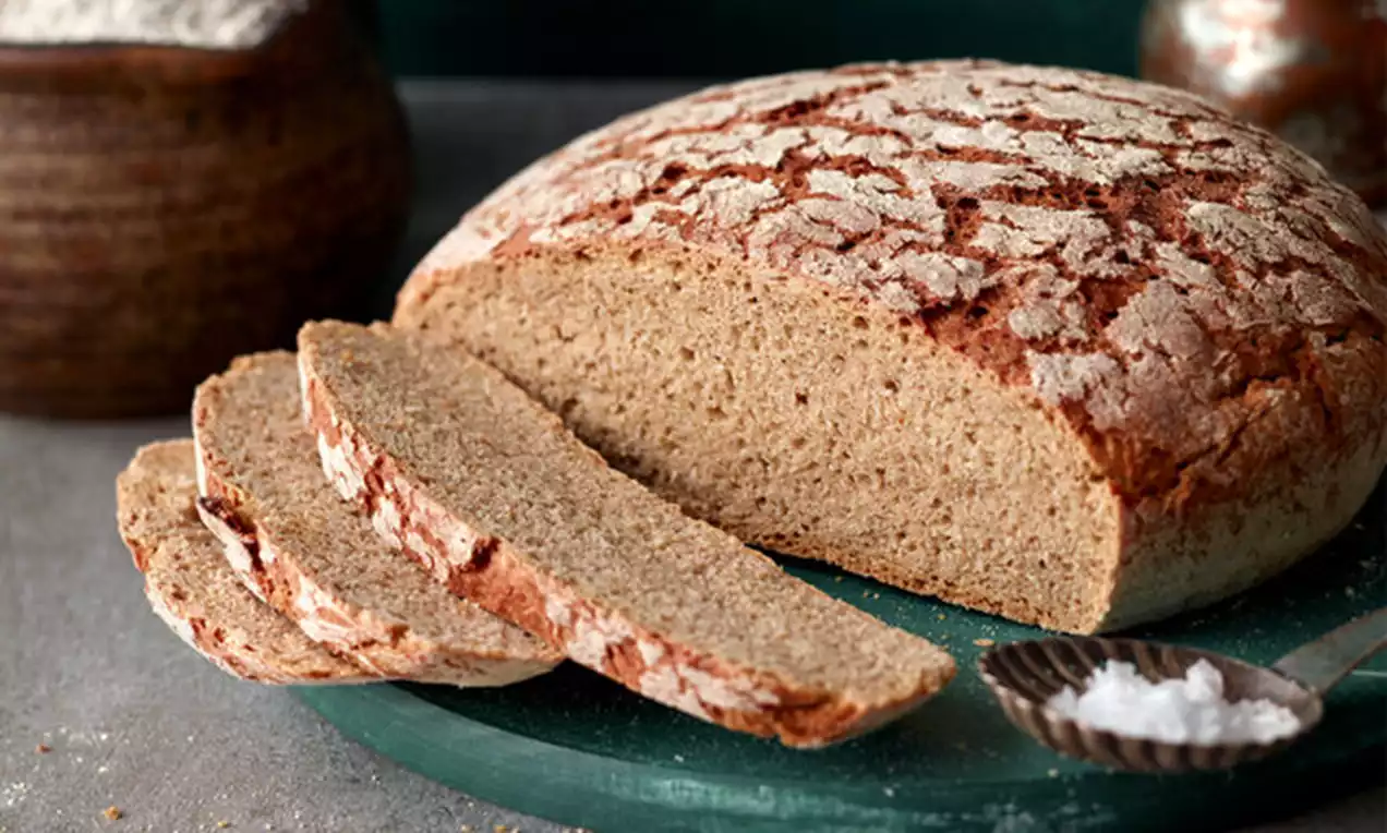Pain au levain brun rustique avec une croûte craquelée poudrée de farine, tranches épaisses et moelleuses disposées sur un plateau vert