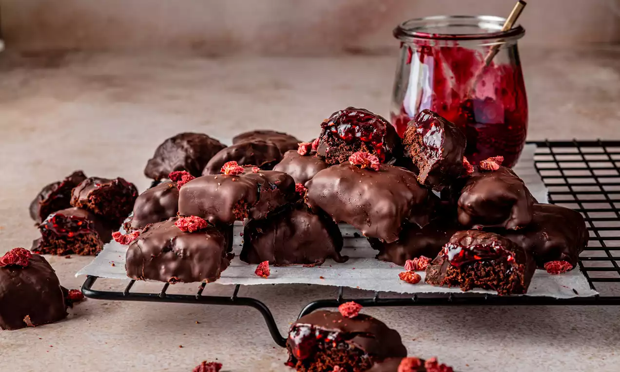 Donkere chocoladebonbons met een glanzende laag, gevuld met jam en brownie en bestrooid met rode kruimels op een metalen rek met pot jam