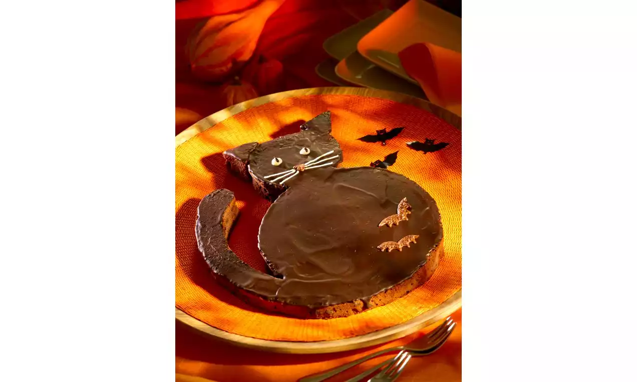 Chocoladekat met glanzend zwarte glazuurlaag, witte snoetdetails en vleermuisdecoratie op een oranje bord met warme achtergrondtinten