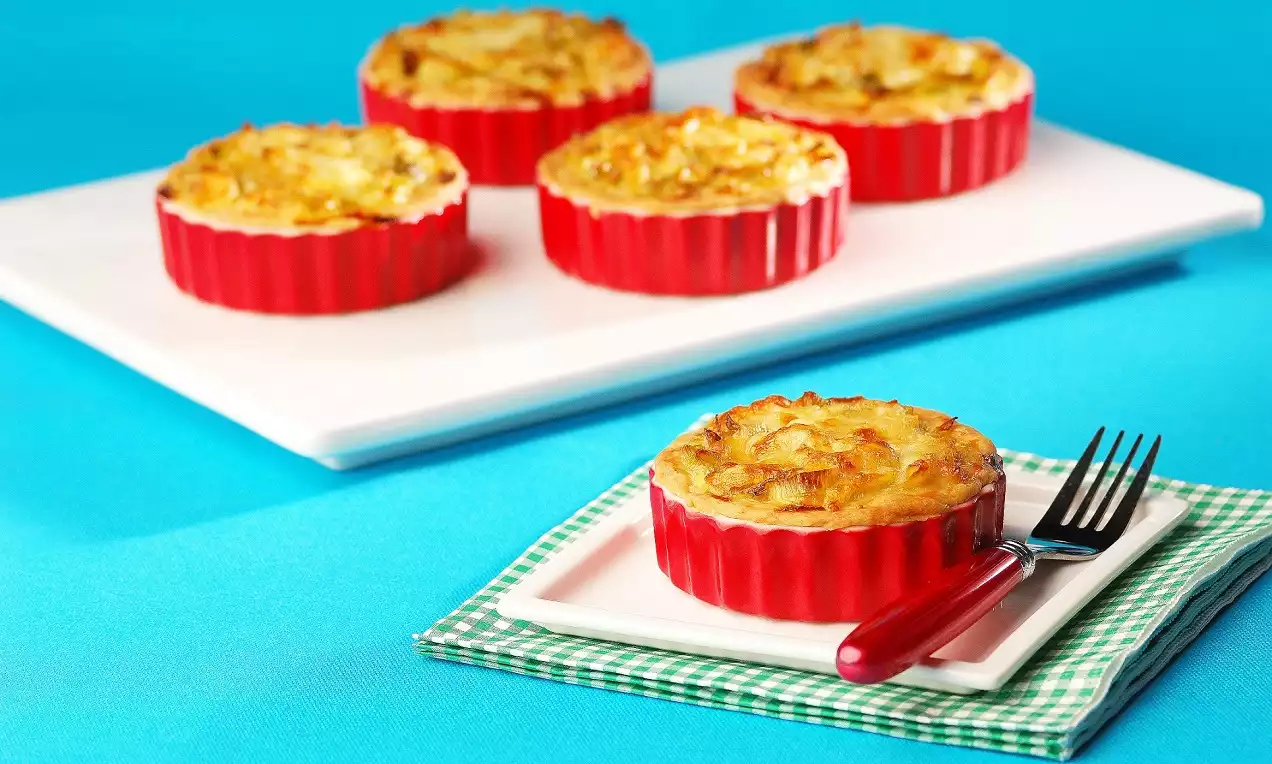 Kırmızı seramik kaplarda altın rengi, hafif kabarmış pırasalı kişler, bir tanesi kare beyaz tabakta çatal ile yeşil ekoseli örtüde