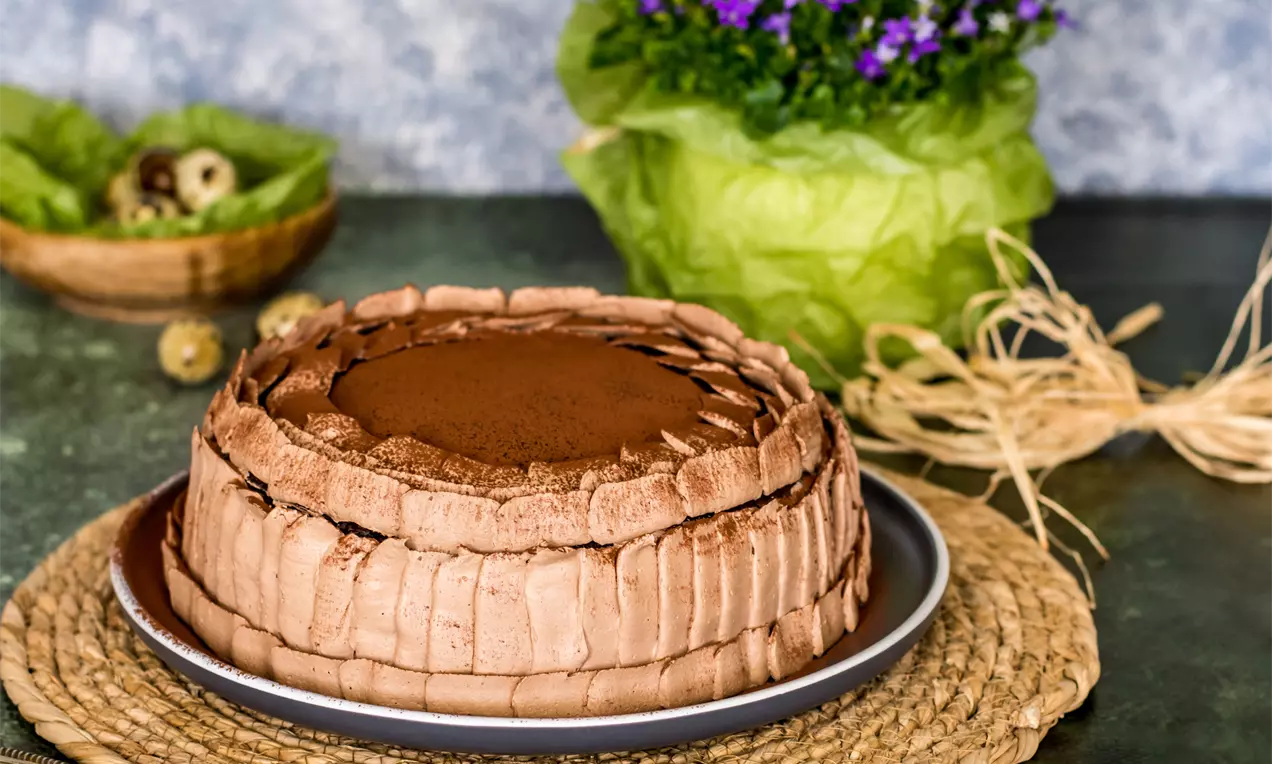 Торта с пластове от какаови палачинки и крем, с гладка какаова повърхност и ръбове от сгънати палачинки върху плоска чиния