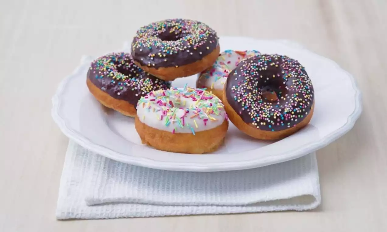 Goudbruine donuts met glanzend chocolade- en witte glazuurlaag, kleurrijke sprinkels op een wit bord met zacht beige ondergrond