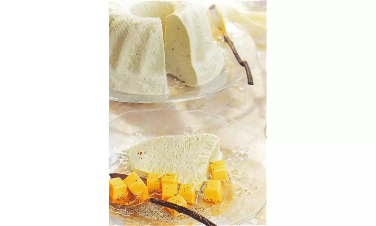 Glace vanillée blanc crème en forme de couronne avec une tranche servie sur une assiette, entourée de cubes orangés et gousses de vanille